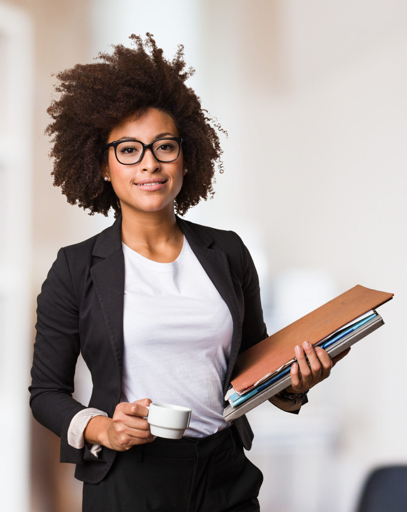 professional black woman holds files and coffee cup in an office setting